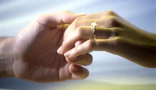 Close-up of a man's hand holding a woman's hand with an engagement ring
